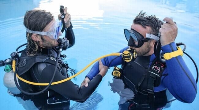 Two scuba divers preparing their equipment while floating on the water surface before a dive.