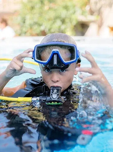 Young scuba diver at the water surface wearing a dive mask and regulator.