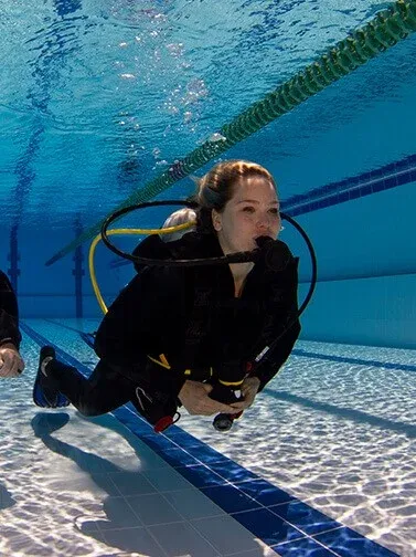 Person practising scuba diving skills in a swimming pool while wearing full diving equipment.